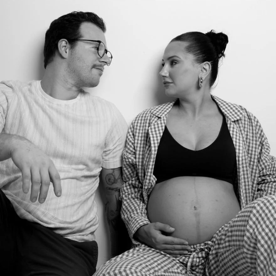 Casal em ensaio de gestante em preto e branco, olhando-se com a mão sobre a barriga